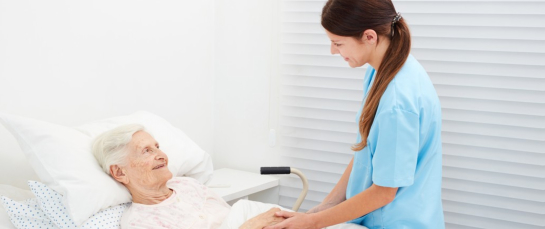 Senior lying in bed in hospice and talking to a caring caregiver